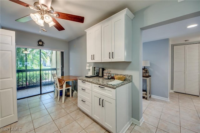 kitchen featuring light tile patterned floors, white cabinets, ceiling fan, light stone countertops, and baseboards