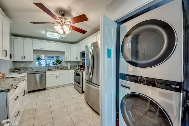 kitchen featuring white cabinets, stacked washer and clothes dryer, appliances with stainless steel finishes, light stone counters, and light tile patterned flooring