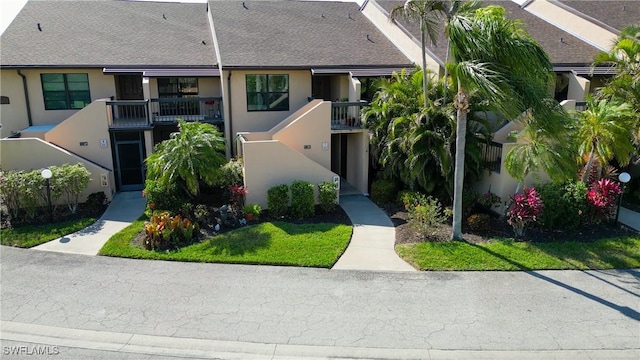 view of front of house featuring a shingled roof, a balcony, and stucco siding