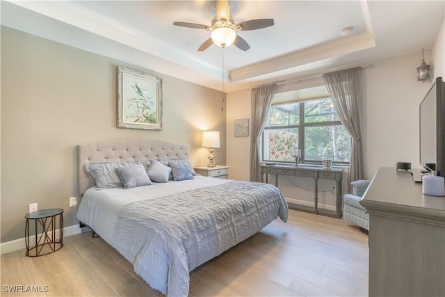 bedroom featuring a tray ceiling, light wood-type flooring, a ceiling fan, and baseboards