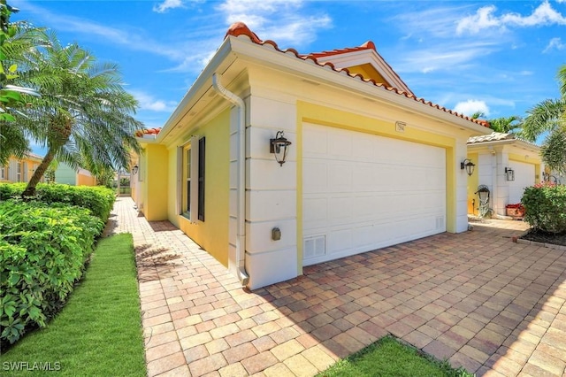 view of side of property featuring stucco siding, an attached garage, and a tile roof