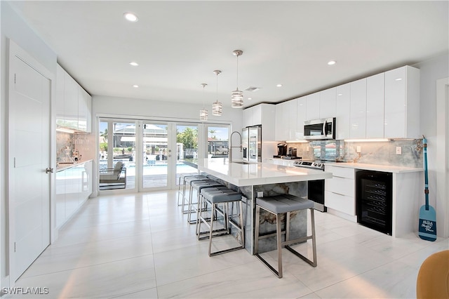 kitchen featuring a kitchen island with sink, hanging light fixtures, wine cooler, appliances with stainless steel finishes, and white cabinets