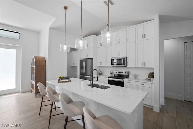 kitchen featuring an island with sink, stainless steel appliances, sink, white cabinets, and pendant lighting