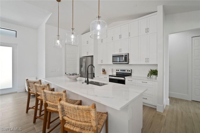 kitchen with white cabinetry, a center island with sink, stainless steel appliances, a breakfast bar area, and pendant lighting