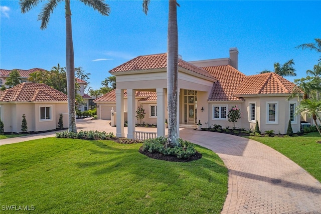 mediterranean / spanish house with decorative driveway, a front yard, a tile roof, and stucco siding