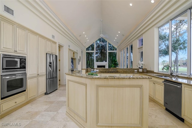 kitchen with cream cabinets, light stone counters, stainless steel appliances, and a sink