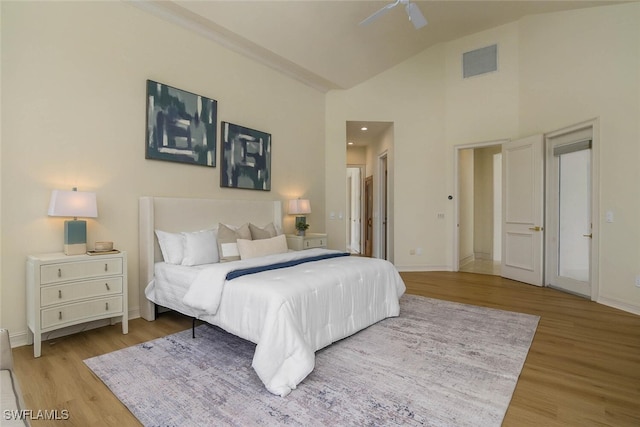 bedroom featuring light wood-style floors, baseboards, visible vents, and high vaulted ceiling