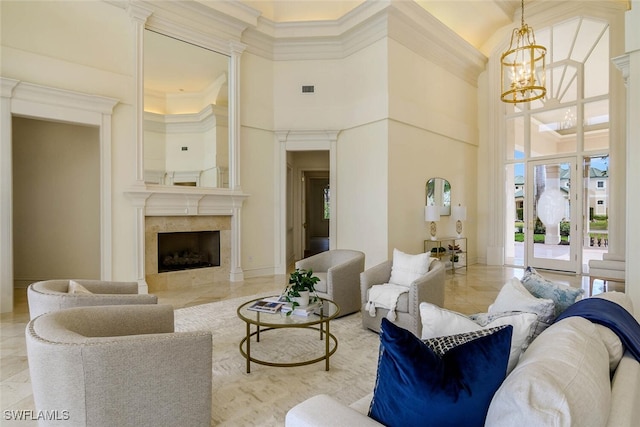 living area with ornamental molding, a towering ceiling, a high end fireplace, and an inviting chandelier