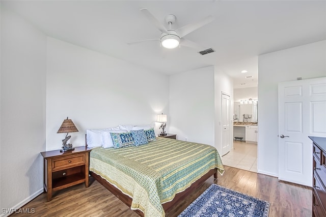 bedroom with ensuite bathroom, a ceiling fan, visible vents, baseboards, and light wood finished floors