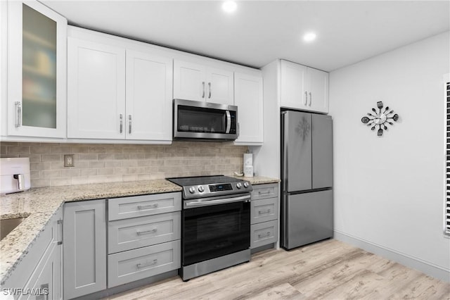 kitchen with glass insert cabinets, light wood-style flooring, appliances with stainless steel finishes, and backsplash