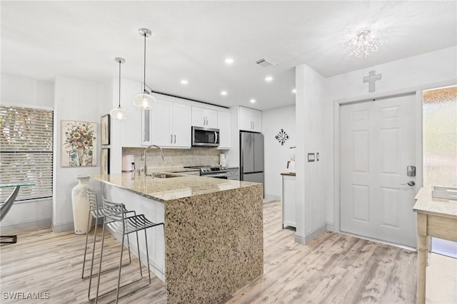 kitchen featuring stainless steel appliances, light wood-style flooring, decorative backsplash, a sink, and light stone countertops