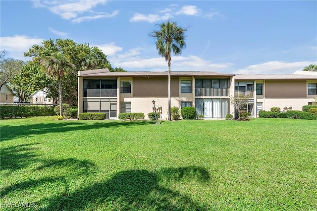 rear view of property with a lawn, a sunroom, and stucco siding