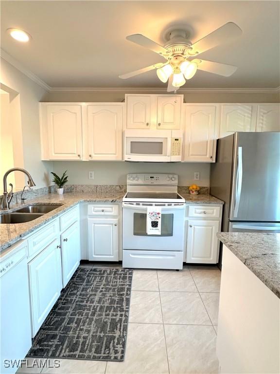 kitchen featuring white appliances, a sink, white cabinets, light stone countertops, and crown molding