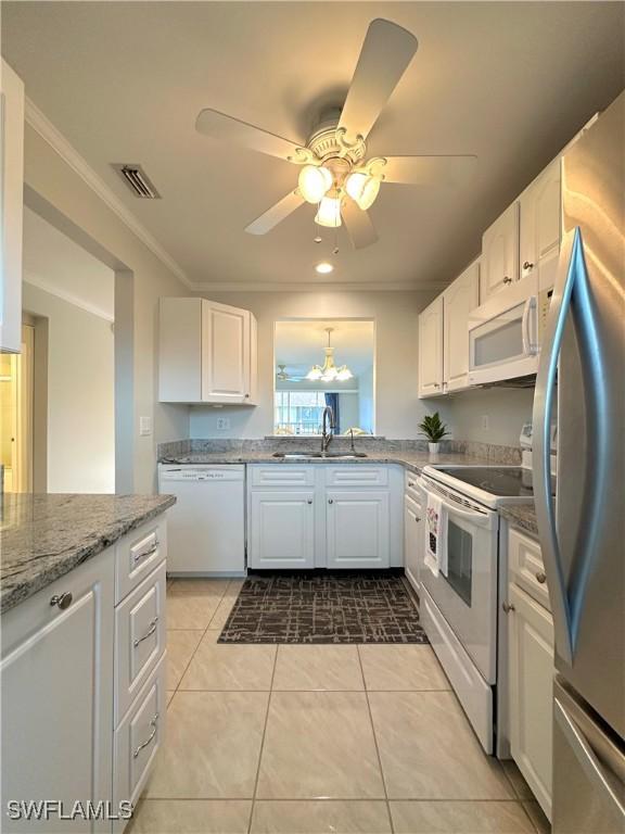 kitchen featuring white appliances, visible vents, white cabinets, crown molding, and a sink