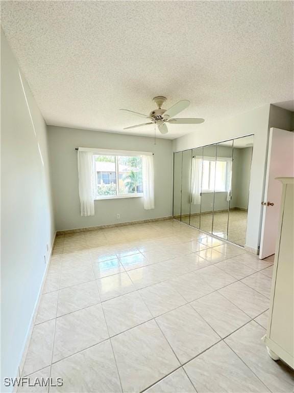 unfurnished bedroom with multiple windows, a textured ceiling, baseboards, light tile patterned flooring, and a closet