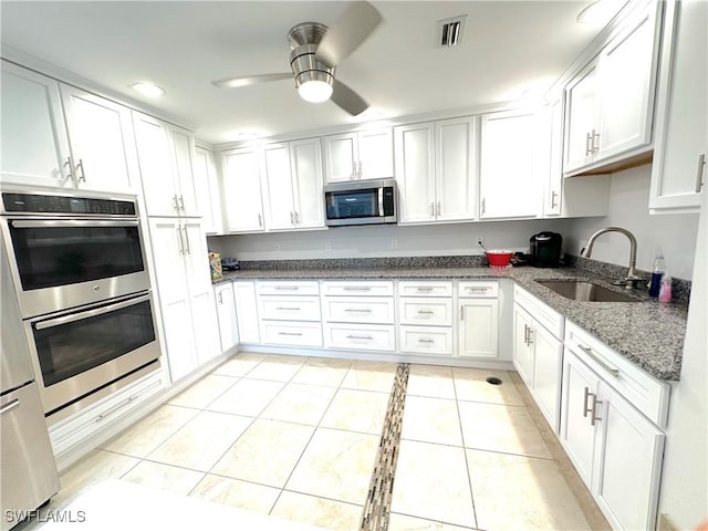 kitchen featuring stainless steel appliances, a sink, white cabinetry, ceiling fan, and dark stone countertops