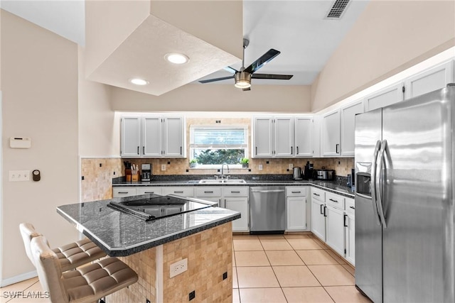 kitchen featuring visible vents, dark stone countertops, stainless steel appliances, white cabinetry, and a sink