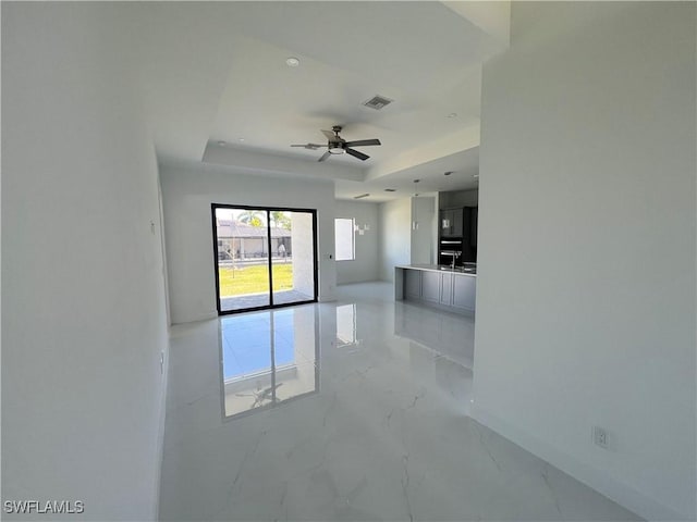 empty room with a tray ceiling, marble finish floor, visible vents, ceiling fan, and baseboards