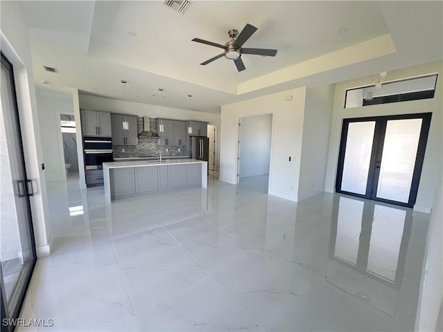 kitchen featuring a raised ceiling, freestanding refrigerator, light countertops, gray cabinetry, and wall chimney range hood