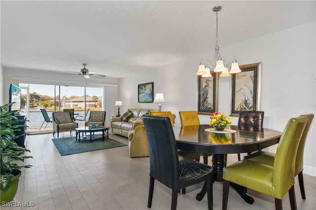 dining space with a textured ceiling, wood finished floors, and ceiling fan with notable chandelier