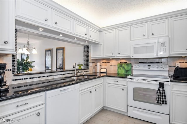 kitchen featuring white appliances, tasteful backsplash, white cabinets, an inviting chandelier, and a sink