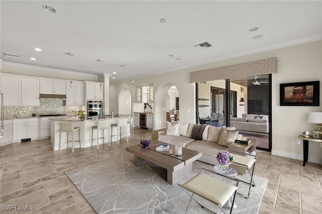 living room featuring visible vents, arched walkways, baseboards, and ornamental molding