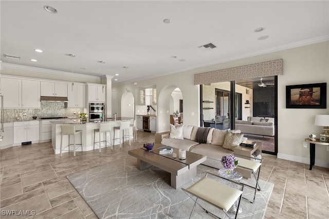 living area with crown molding, arched walkways, visible vents, and recessed lighting