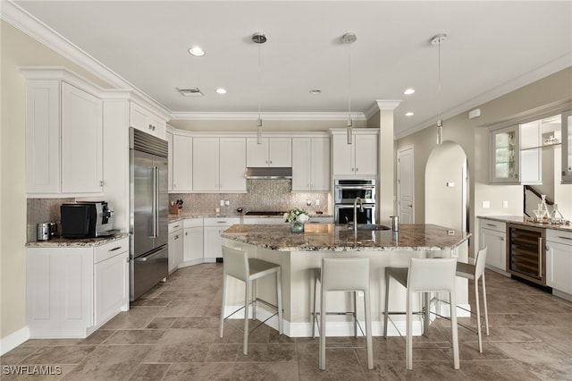 kitchen with ornamental molding, beverage cooler, under cabinet range hood, arched walkways, and appliances with stainless steel finishes