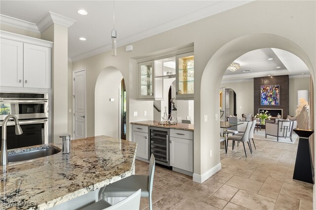 kitchen featuring beverage cooler, a sink, stainless steel double oven, crown molding, and light stone countertops