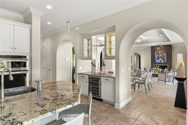 kitchen with ornamental molding, light stone countertops, beverage cooler, stainless steel double oven, and arched walkways