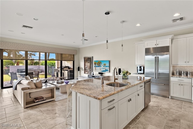 kitchen featuring a kitchen island with sink, crown molding, a sink, white cabinets, and stainless steel appliances