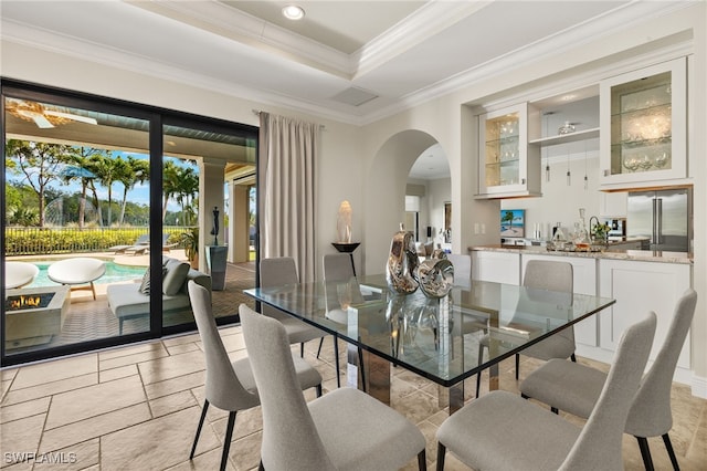 dining area with ornamental molding, indoor wet bar, arched walkways, stone tile flooring, and a raised ceiling