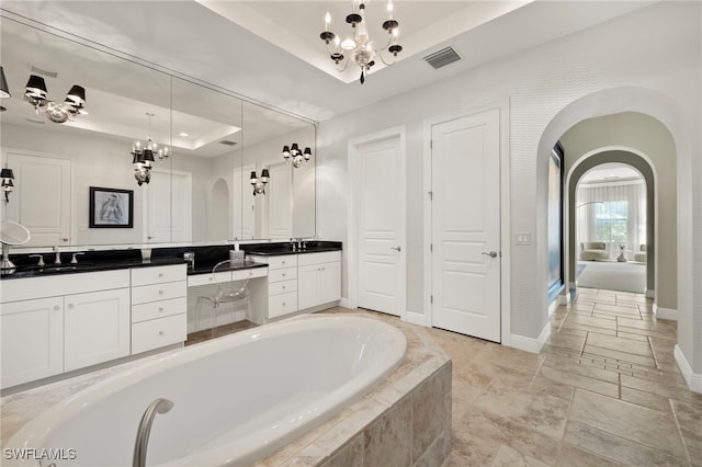 bathroom with a notable chandelier, a raised ceiling, vanity, baseboards, and a bath