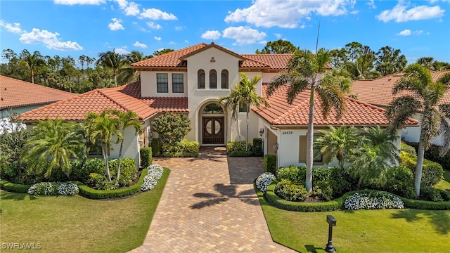mediterranean / spanish house featuring a front lawn, a tile roof, and stucco siding