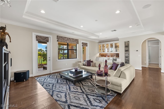 living area with arched walkways, dark wood-style floors, and a tray ceiling