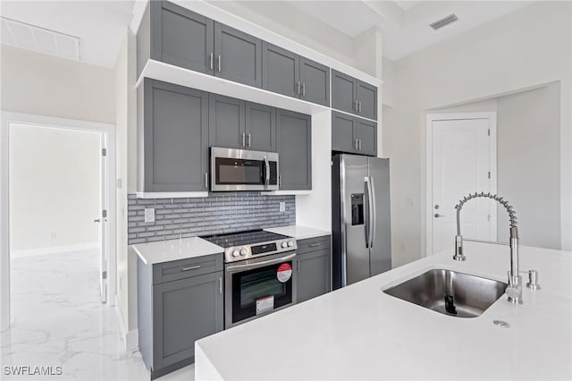 kitchen featuring appliances with stainless steel finishes, marble finish floor, light countertops, gray cabinetry, and a sink