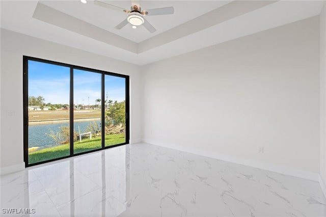 spare room with a tray ceiling, marble finish floor, a water view, and baseboards