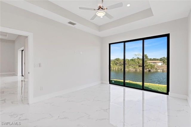 empty room featuring a water view, marble finish floor, baseboards, and a raised ceiling