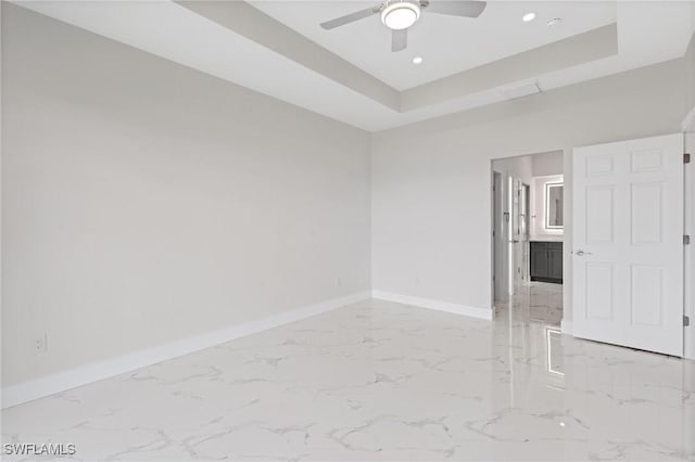 unfurnished room featuring marble finish floor, a tray ceiling, a ceiling fan, and baseboards