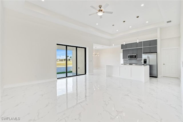 unfurnished living room featuring baseboards, visible vents, a raised ceiling, marble finish floor, and ceiling fan with notable chandelier