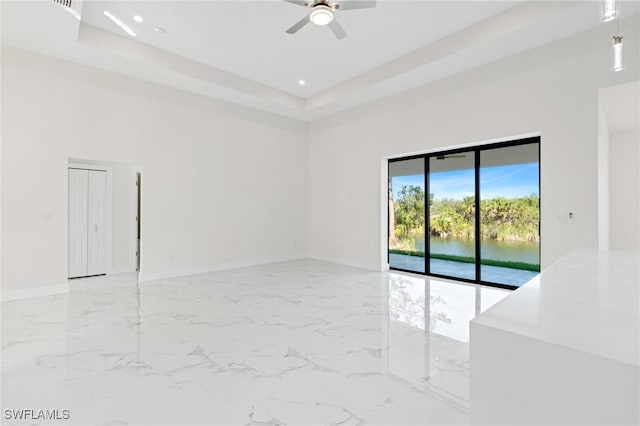 empty room featuring marble finish floor, a water view, a raised ceiling, and baseboards