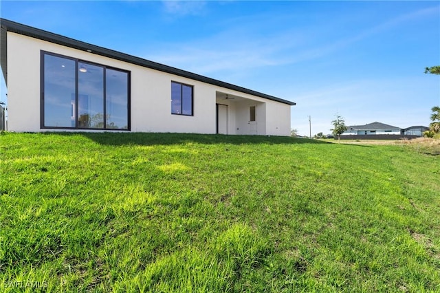 rear view of house with a lawn and stucco siding