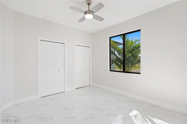 unfurnished bedroom featuring marble finish floor, a ceiling fan, baseboards, and two closets