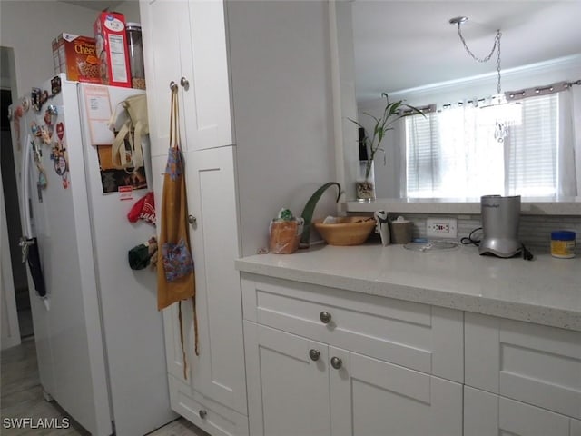 kitchen with light stone counters, freestanding refrigerator, and white cabinetry