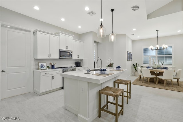 kitchen featuring a kitchen island with sink, decorative light fixtures, appliances with stainless steel finishes, white cabinets, and a breakfast bar area