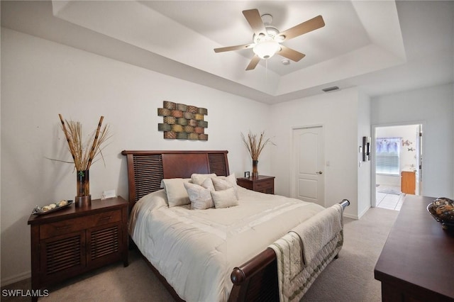 bedroom with a raised ceiling, ceiling fan, ensuite bath, and light colored carpet