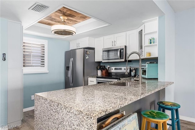 kitchen featuring white cabinetry, kitchen peninsula, stainless steel appliances, light stone countertops, and a raised ceiling