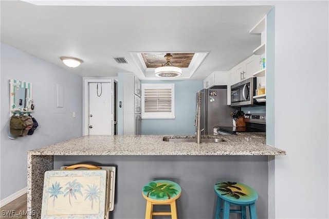 kitchen featuring stainless steel appliances, a raised ceiling, white cabinetry, a kitchen bar, and kitchen peninsula