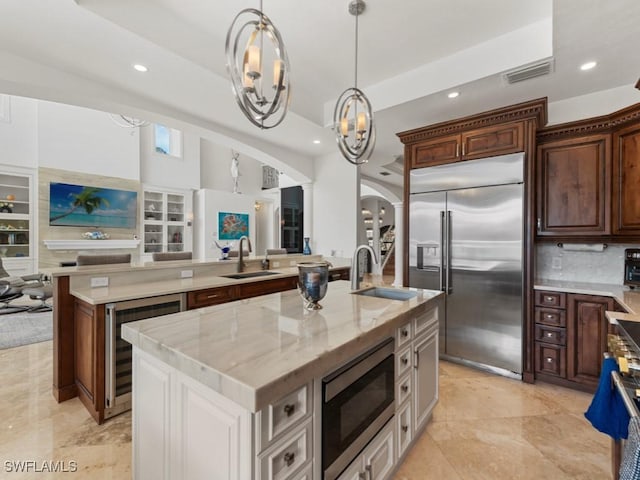 kitchen with arched walkways, built in appliances, wine cooler, and a sink