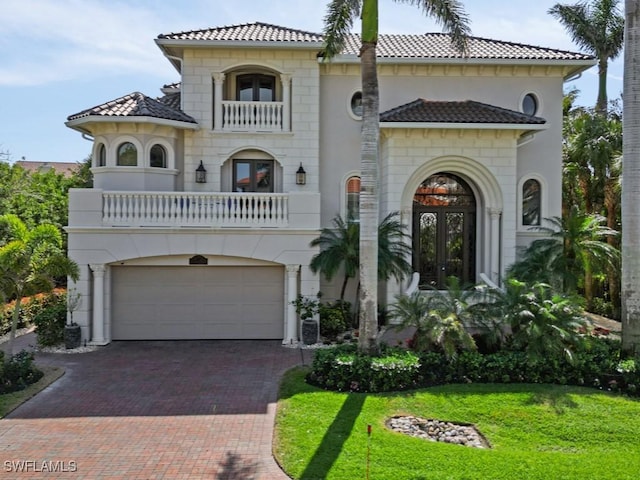 mediterranean / spanish-style house featuring a balcony, an attached garage, french doors, a tile roof, and decorative driveway